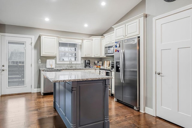 kitchen featuring lofted ceiling, light stone counters, stainless steel appliances, a kitchen island, and white cabinets