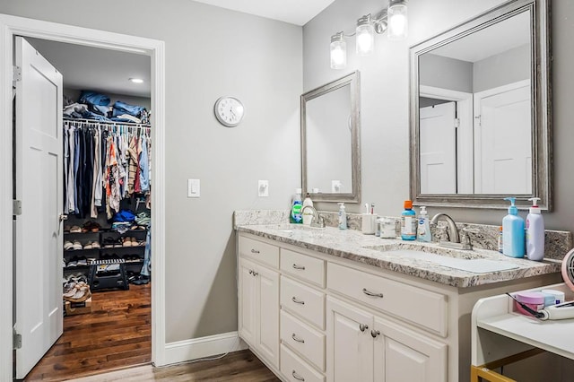 bathroom with a sink, double vanity, wood finished floors, and a walk in closet