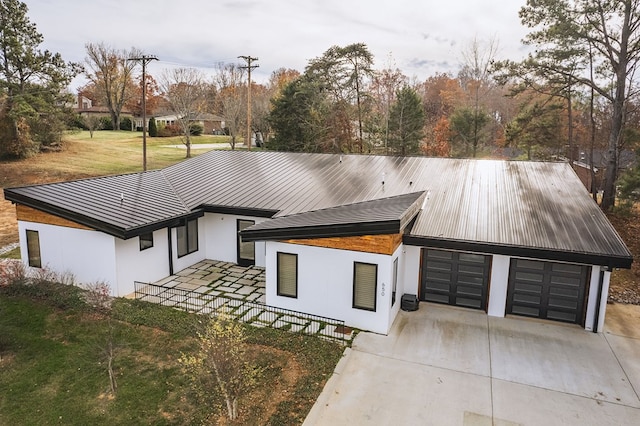 view of front of house with stucco siding, concrete driveway, metal roof, a garage, and a front lawn