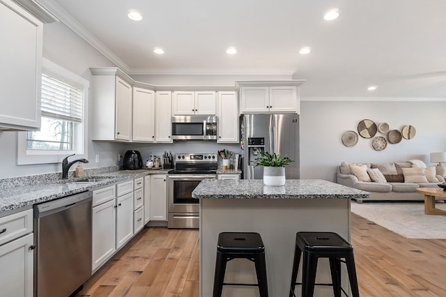 kitchen featuring a sink, white cabinetry, open floor plan, appliances with stainless steel finishes, and light stone countertops