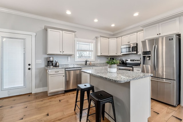 kitchen with stainless steel appliances, ornamental molding, white cabinets, a sink, and a kitchen island