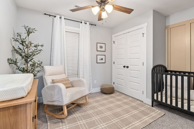 carpeted bedroom featuring a closet, visible vents, a ceiling fan, a crib, and baseboards