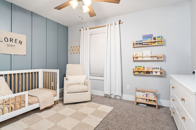 bedroom with a nursery area, baseboards, ceiling fan, and carpet