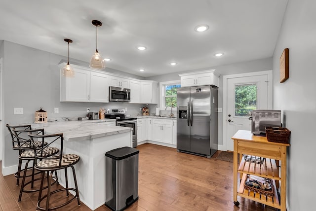 kitchen with stainless steel appliances, hanging light fixtures, white cabinets, light stone countertops, and a peninsula