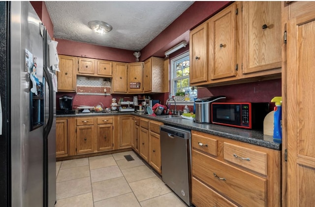 kitchen with dark countertops, appliances with stainless steel finishes, brown cabinetry, light tile patterned flooring, and a textured ceiling