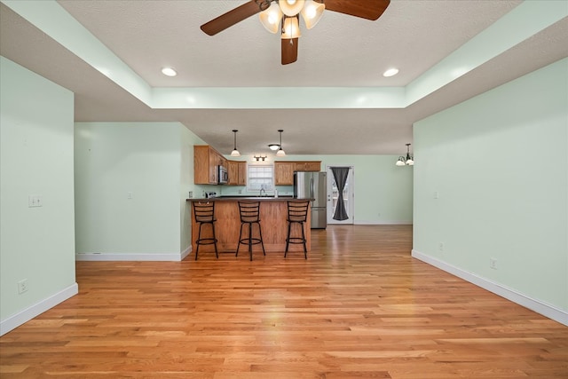 kitchen with brown cabinetry, appliances with stainless steel finishes, open floor plan, a peninsula, and pendant lighting