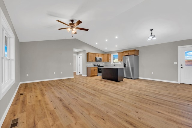 kitchen featuring appliances with stainless steel finishes, open floor plan, a center island, decorative light fixtures, and light countertops