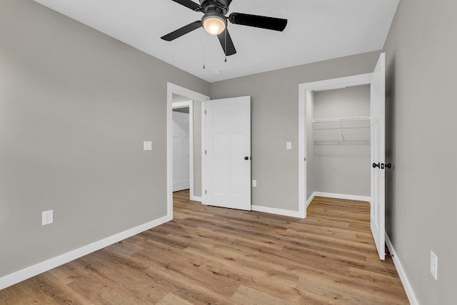 unfurnished bedroom with a ceiling fan, baseboards, a closet, light wood finished floors, and a walk in closet