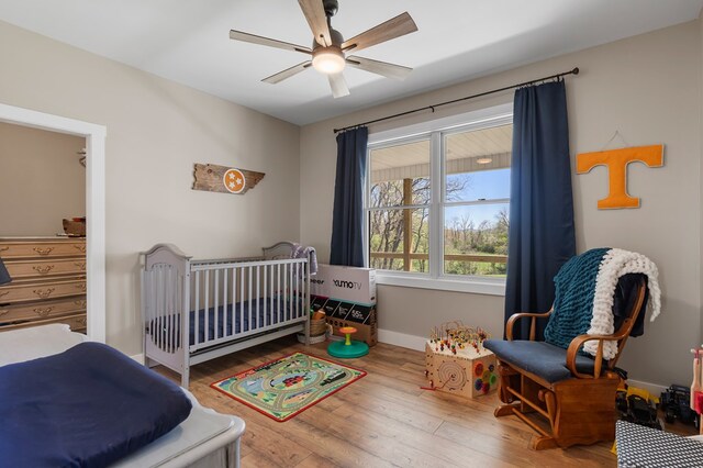 bedroom featuring a crib, wood finished floors, a ceiling fan, and baseboards