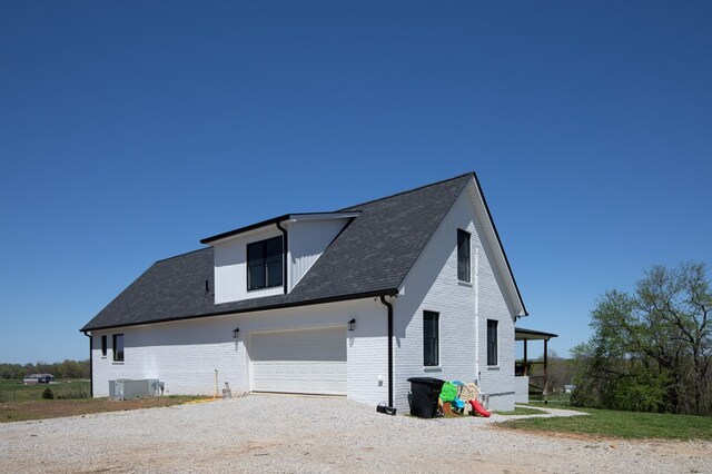 view of property exterior with a garage, central AC unit, gravel driveway, and brick siding