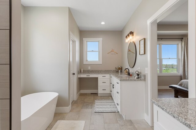 bathroom featuring a freestanding bath, a wealth of natural light, vanity, and baseboards