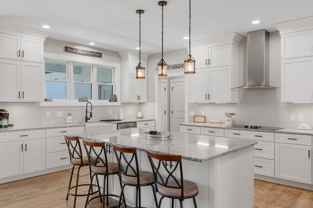 kitchen featuring black electric stovetop, a sink, wall chimney range hood, a center island, and pendant lighting