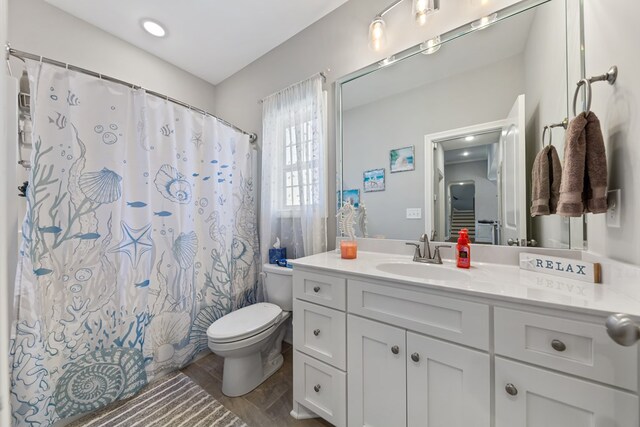 bathroom with toilet, curtained shower, wood finished floors, and vanity