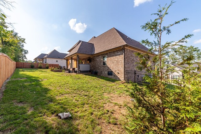 rear view of property featuring roof with shingles, brick siding, a lawn, and a fenced backyard