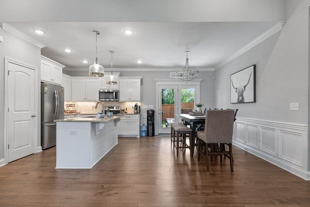 kitchen featuring light stone counters, a kitchen island with sink, white cabinetry, appliances with stainless steel finishes, and pendant lighting