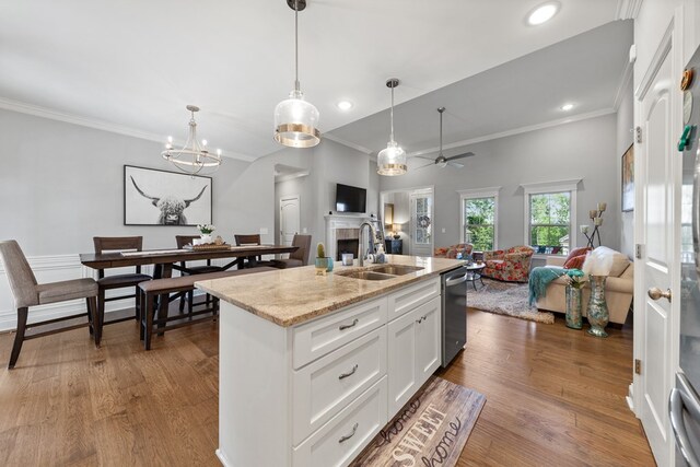 kitchen with a center island with sink, white cabinets, open floor plan, light stone countertops, and a sink