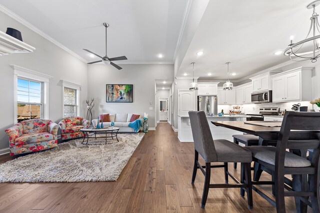 dining space with baseboards, dark wood finished floors, ornamental molding, ceiling fan with notable chandelier, and recessed lighting