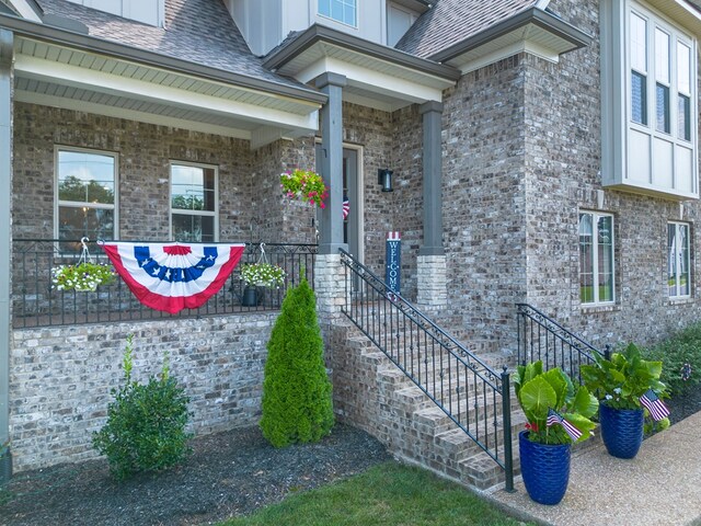 entrance to property featuring a shingled roof and brick siding