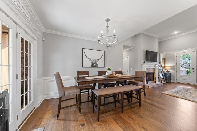 dining area with dark wood-type flooring, a fireplace with raised hearth, ornamental molding, and an inviting chandelier