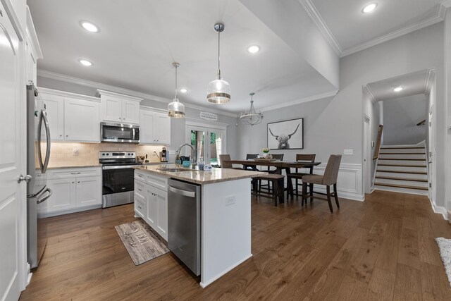 kitchen featuring hanging light fixtures, appliances with stainless steel finishes, a center island with sink, and white cabinetry