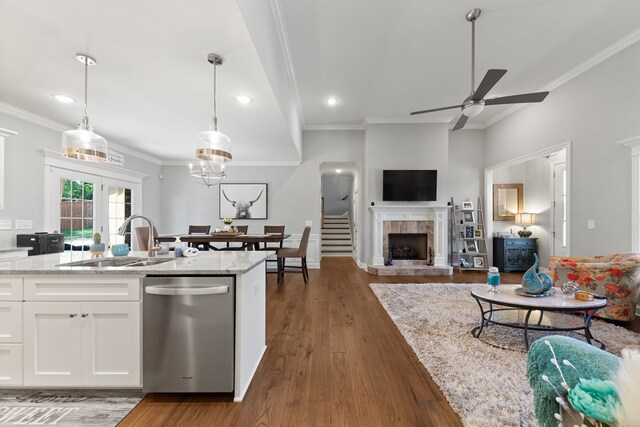 kitchen with light stone counters, a sink, white cabinets, dishwasher, and decorative light fixtures