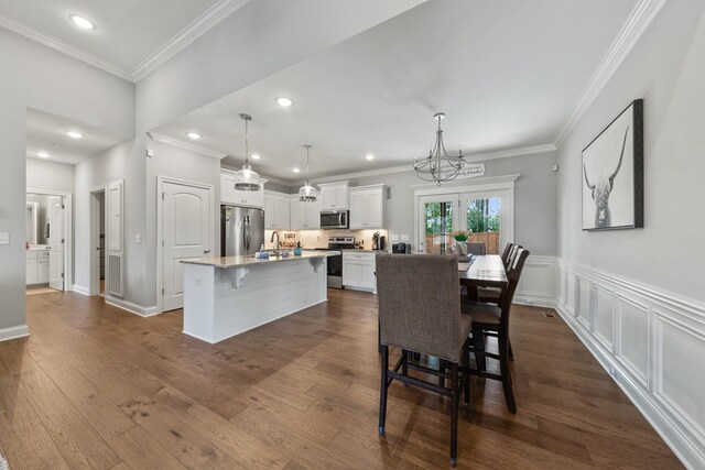 dining area featuring a wainscoted wall, ornamental molding, dark wood-type flooring, a decorative wall, and a notable chandelier