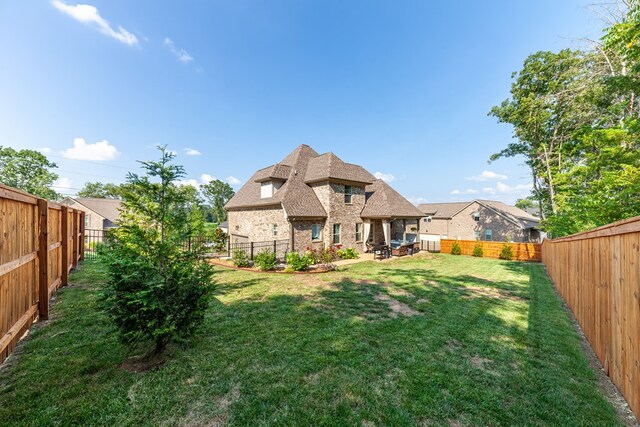 back of property with stone siding, a fenced backyard, and a lawn