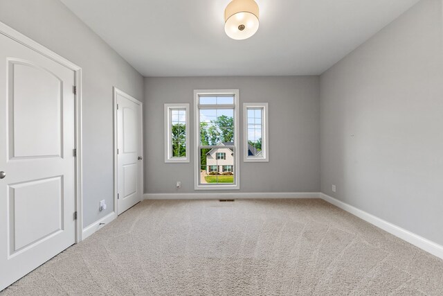 spare room featuring light colored carpet, visible vents, and baseboards