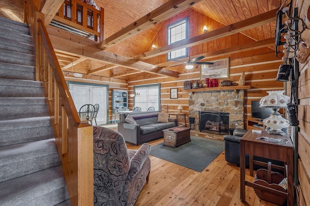 living room featuring beamed ceiling, wood finished floors, stairs, a stone fireplace, and wood walls