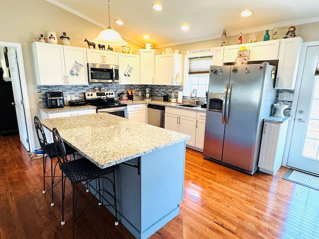 kitchen featuring light wood finished floors, lofted ceiling, appliances with stainless steel finishes, crown molding, and a sink