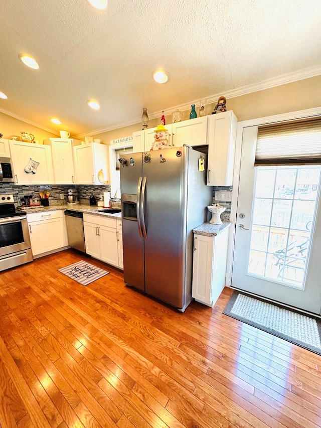 kitchen featuring tasteful backsplash, stainless steel appliances, crown molding, light wood-style floors, and white cabinetry