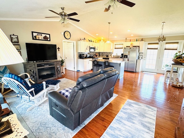 living area with light wood-style flooring, a ceiling fan, vaulted ceiling, and crown molding