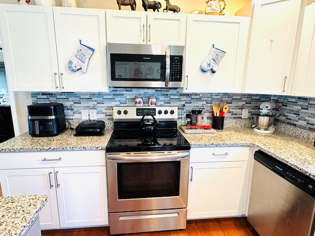 kitchen featuring stainless steel appliances, white cabinets, light stone counters, and tasteful backsplash