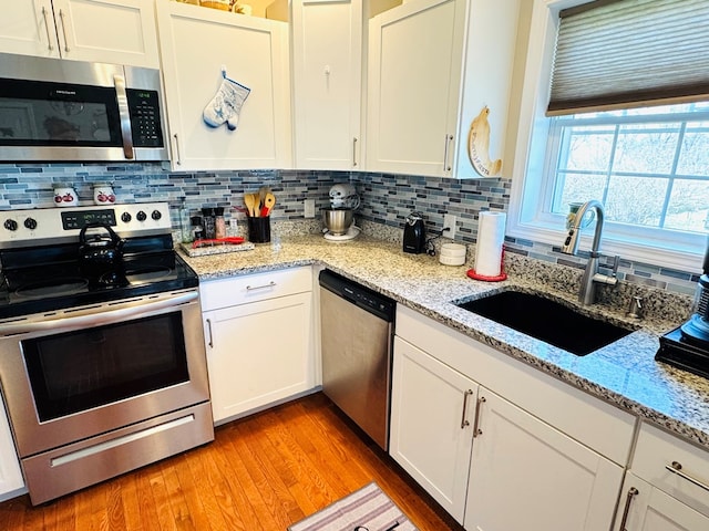 kitchen with stainless steel appliances, backsplash, a sink, and light wood-style flooring