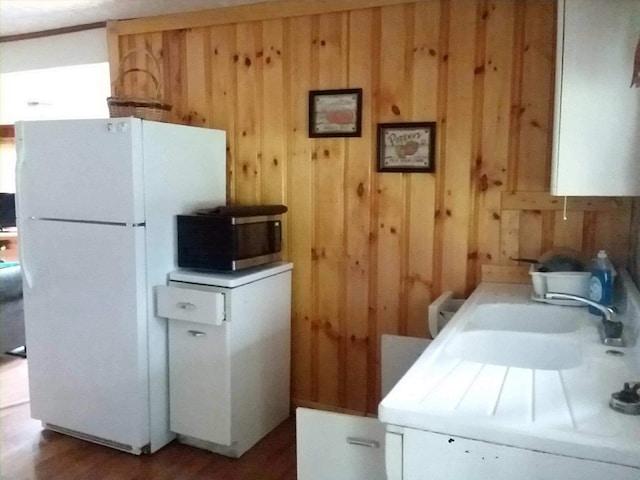 kitchen featuring freestanding refrigerator, light countertops, stainless steel microwave, and wood walls