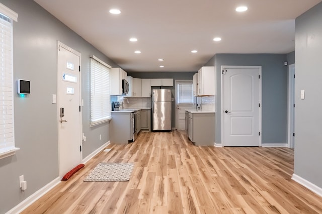 kitchen with stainless steel appliances, tasteful backsplash, light wood-type flooring, and light countertops