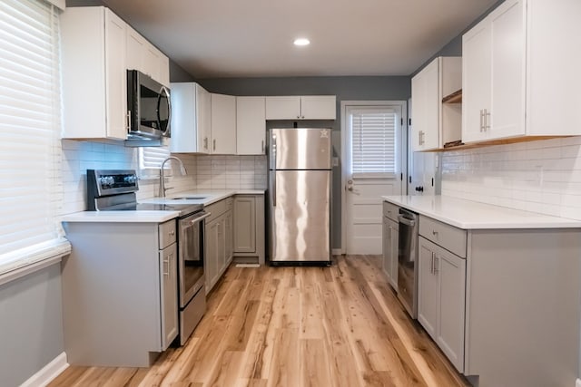 kitchen featuring light wood finished floors, decorative backsplash, stainless steel appliances, light countertops, and a sink