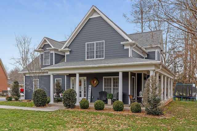 view of front of property featuring covered porch, a trampoline, a front lawn, and roof with shingles