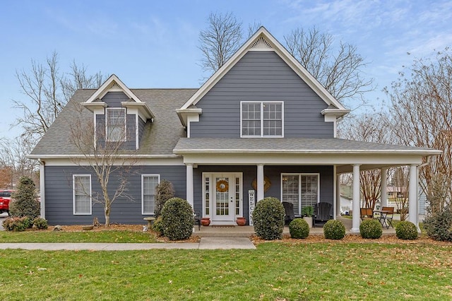 view of front facade with covered porch, roof with shingles, and a front yard