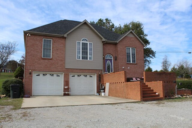 raised ranch featuring concrete driveway, brick siding, an attached garage, and a shingled roof