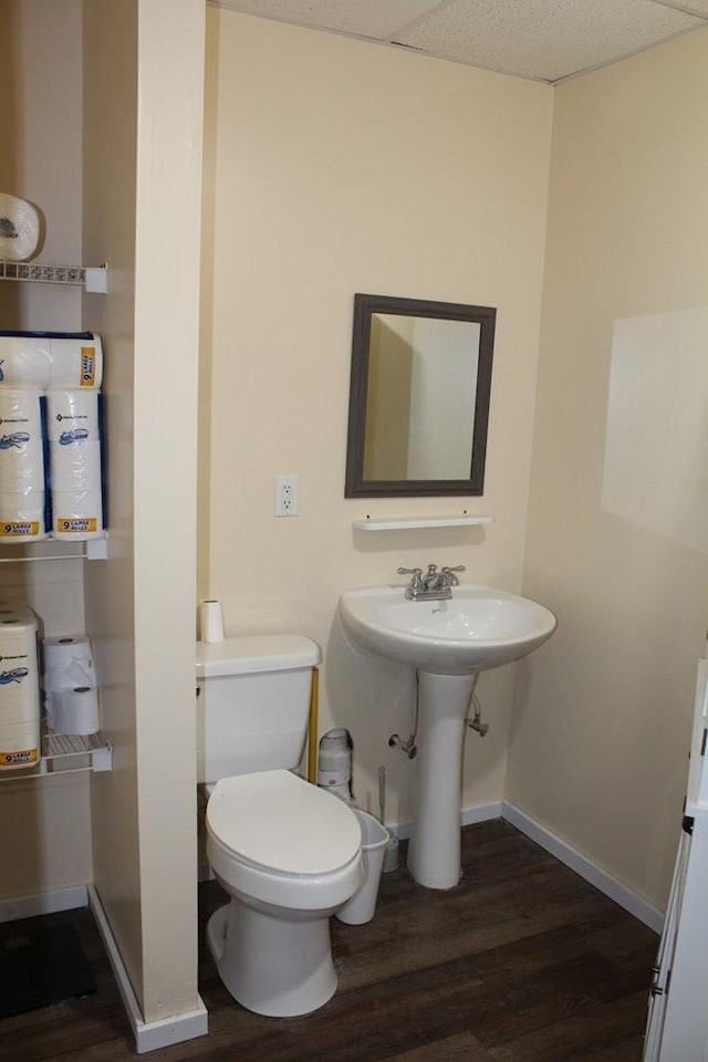 half bathroom featuring toilet, baseboards, a drop ceiling, and wood finished floors