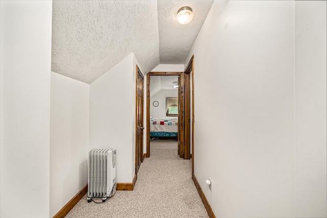 hall featuring radiator heating unit, light carpet, vaulted ceiling, a textured ceiling, and baseboards