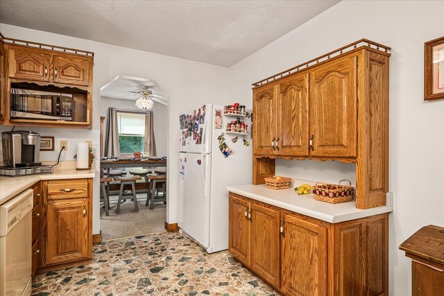 kitchen with a textured ceiling, light countertops, white appliances, and brown cabinetry