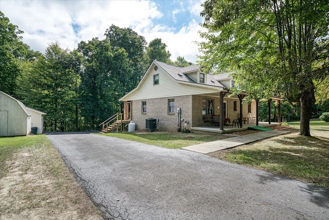 view of side of home featuring brick siding, a storage unit, a porch, central AC unit, and an outdoor structure