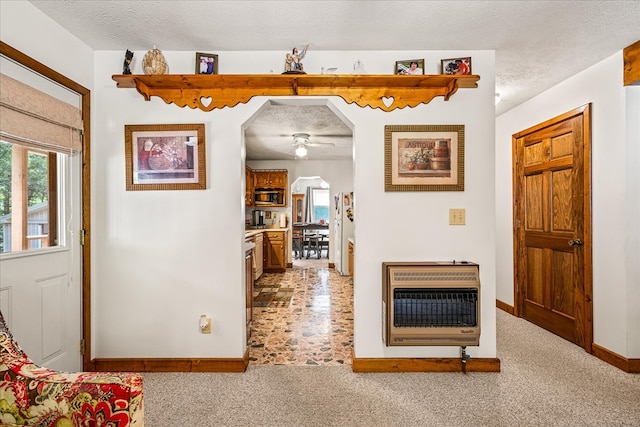 corridor with heating unit, arched walkways, a textured ceiling, and light colored carpet