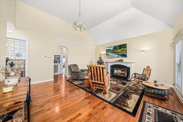 living area with arched walkways, high vaulted ceiling, baseboards, light wood-style floors, and a tiled fireplace