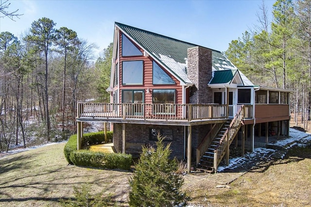 back of property with a sunroom, a chimney, metal roof, stairs, and a deck