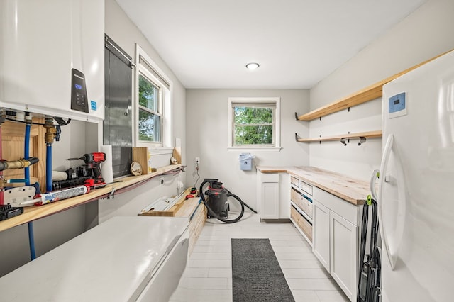 kitchen with open shelves, water heater, freestanding refrigerator, white cabinetry, and wood counters