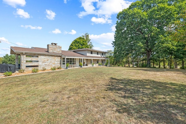 back of house with stone siding, a chimney, a porch, and a yard