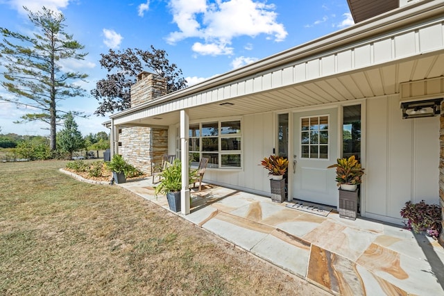 doorway to property featuring a yard, a chimney, stone siding, and board and batten siding